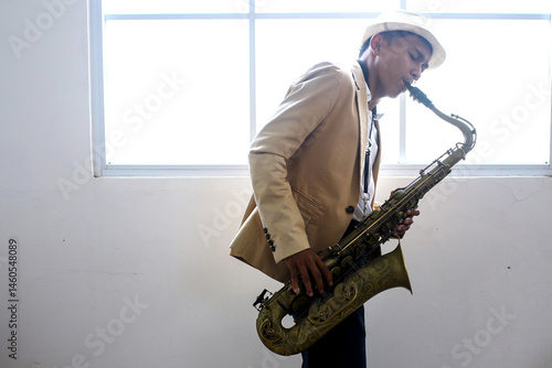 Photography Portrait Of Young Asian Male Musician Playing Saxophone Near Window With Sun Lig