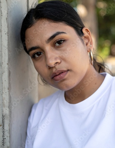 Portrait of South Asian Woman in White Shirt Leaning Against Wall with Calm Expression