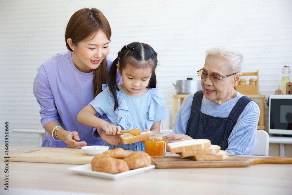 cute little girl putting orange jam on bread toast beside mother and grandmother in the kitchen cute little girl putting orange jam on bread toast beside mother and grandmother in the kitchen