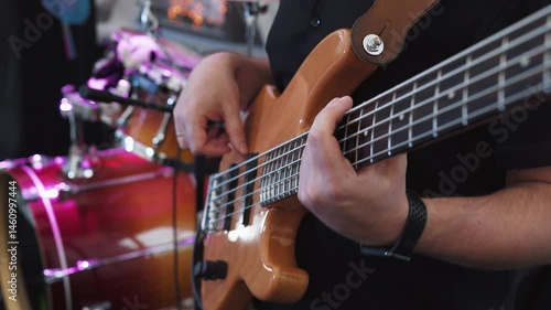 Bass guitarist bassist plays bass guitar during performance at party, concert. Close-up, hands of bass guitarist professionally play pop or rock music on electric bass guitar. Concert lighting