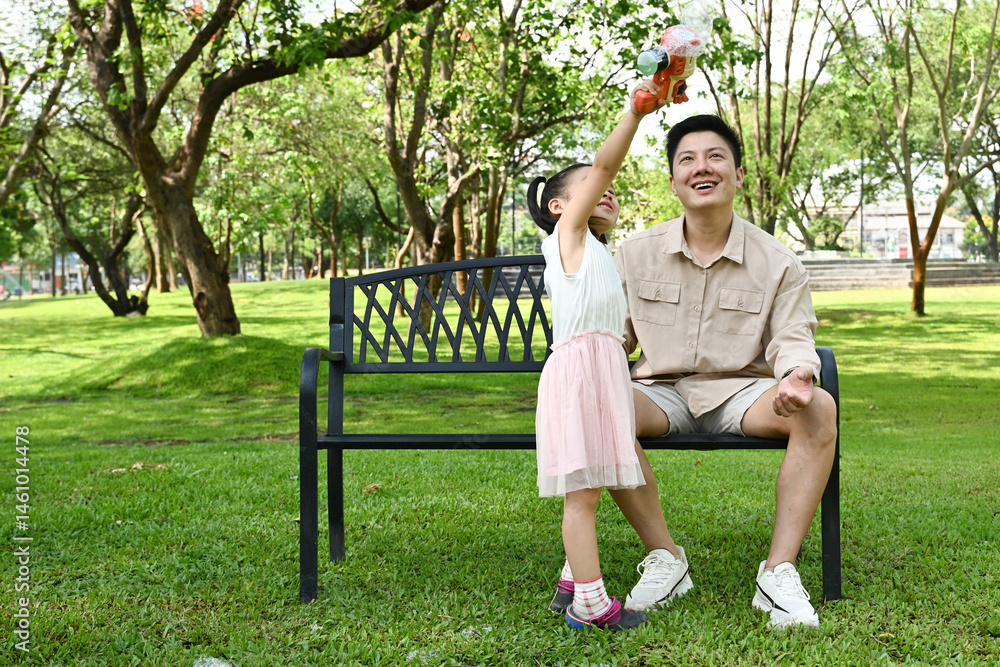 A man and a little girl are sitting on a park bench, Scene is warm and friendly, as the man and the girl seem to be enjoying each other's company.