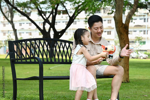 Obraz na płótnie A man and a little girl are sitting on a park bench, Scene is warm and friendly, as the man and the girl seem to be enjoying each other's company. w salonie