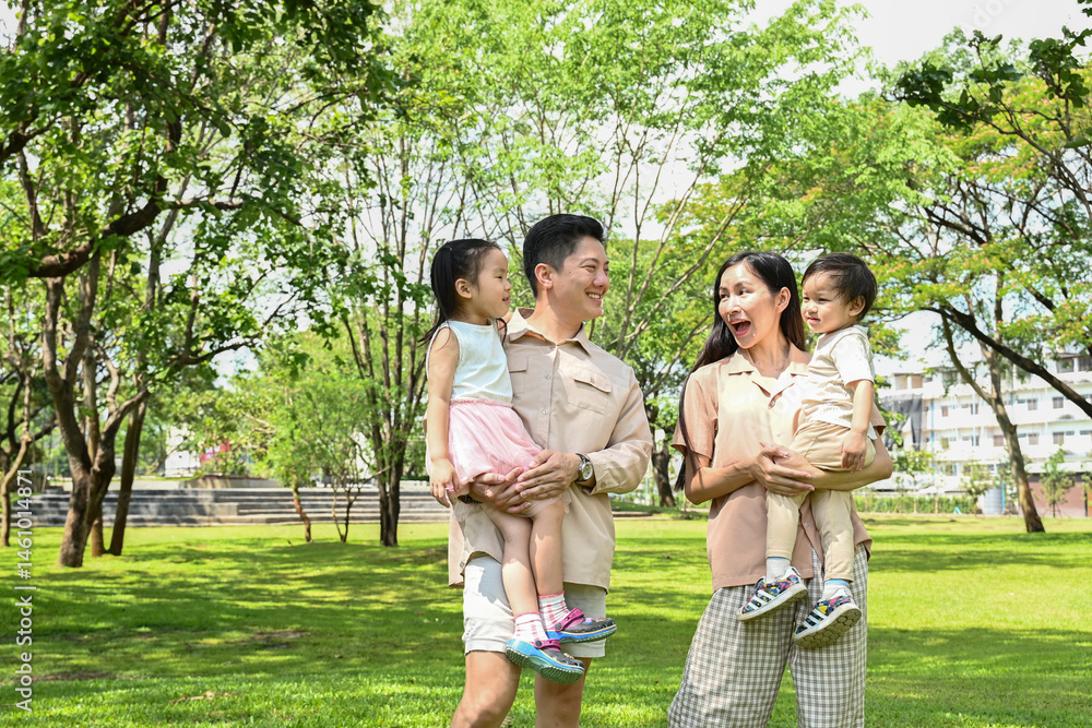 A family of four is walking in a park, the family appears to be happy and enjoying their time together.
