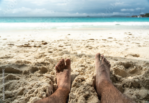 Obraz na płótnie Bare feet resting in warm sand on tropical beach, symbolizing summer relaxation, freedom w salonie