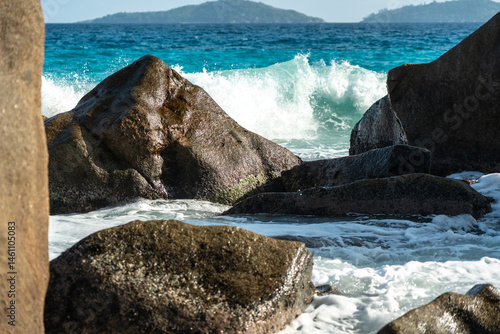Ocean and sea wave crash against rock and water along the beach shore under the blue sky