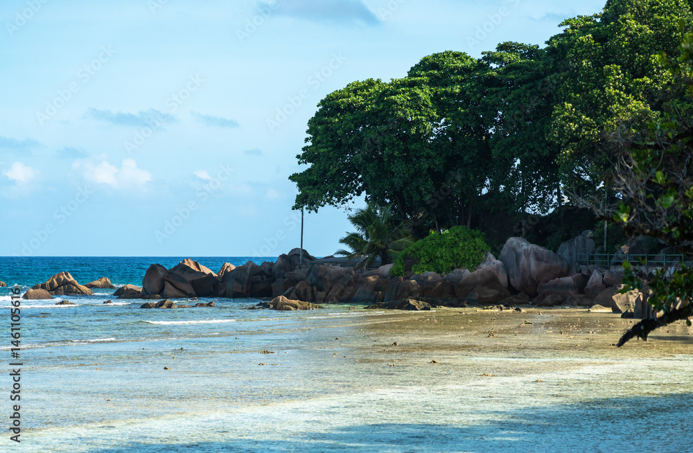 Tropical coastline on La Digue island shows granite boulders, green trees and shallow sea waters