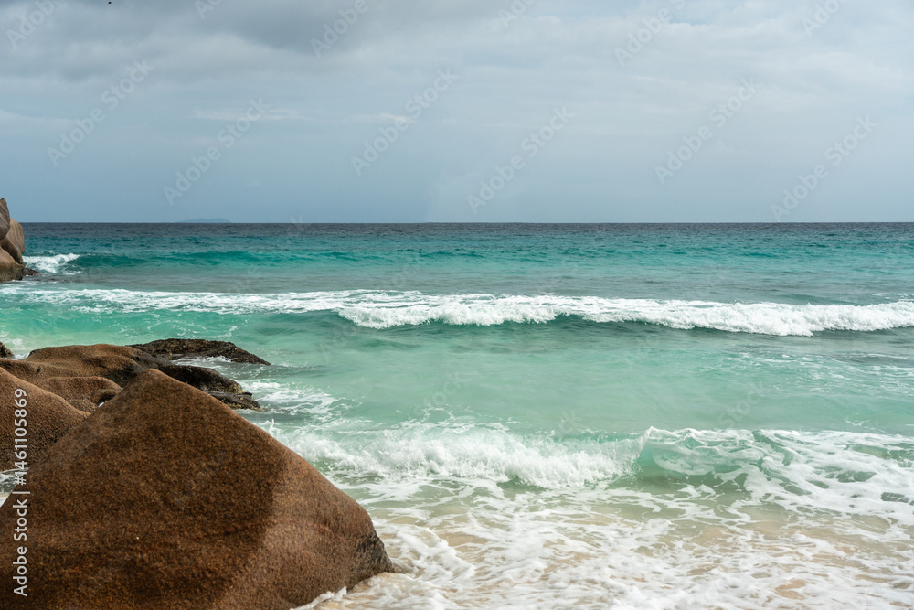 Ocean and sea wave crash against rock and water along the beach shore under the blue sky