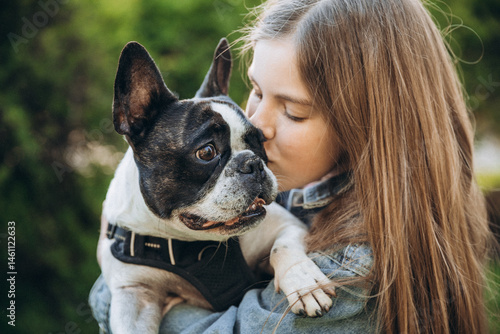 12 year old girl kissing and hugging french bulldog in park.