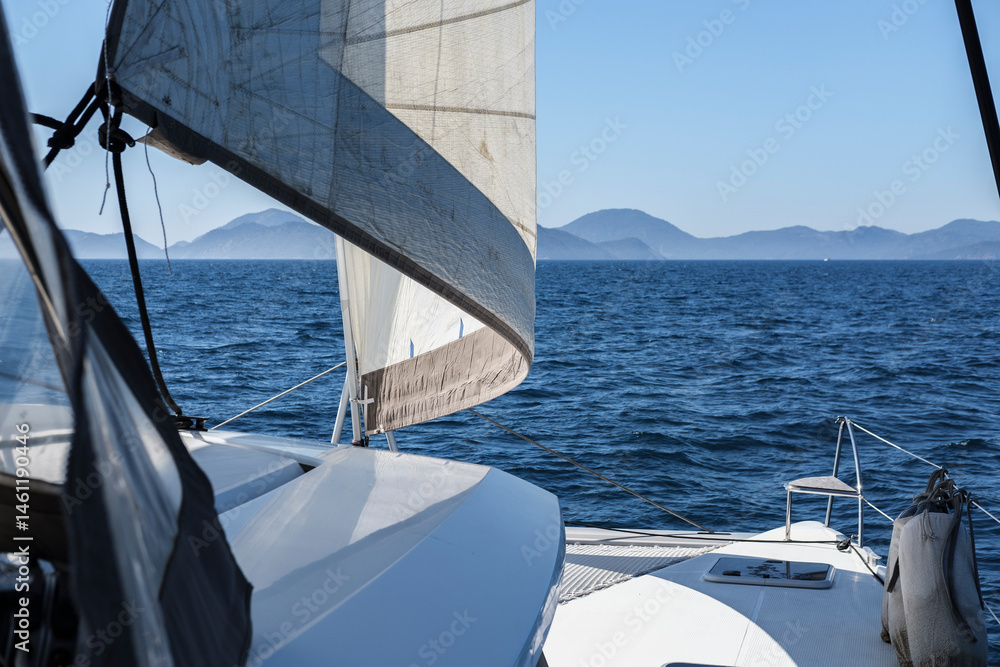Obraz premium open sails, view of catamaran white deck in open blue sea, mountain horizon
