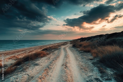 Dramatic sunset over a coastal path.  Golden hues paint the sky above a sandy road leading to the ocean