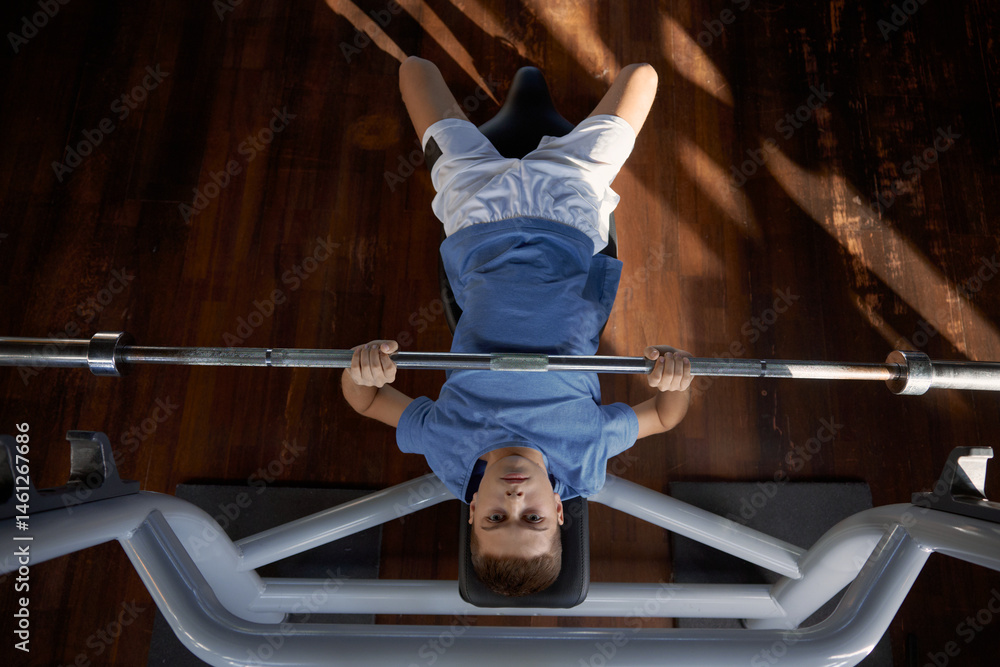 Teenager lifting heavy barbell doing bench press exercise at gym