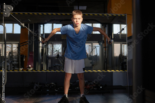 Obraz na płótnie Teenage boy doing exercise using cross over stationery gym machine w salonie
