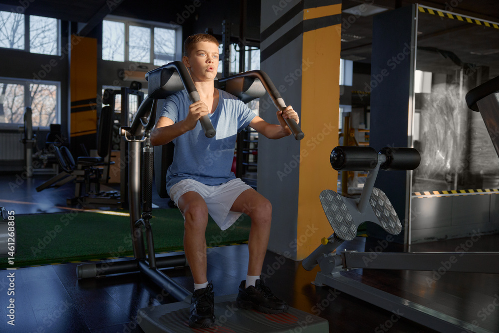 Athletic teenage boy enjoying hard training on fitness machine at gym