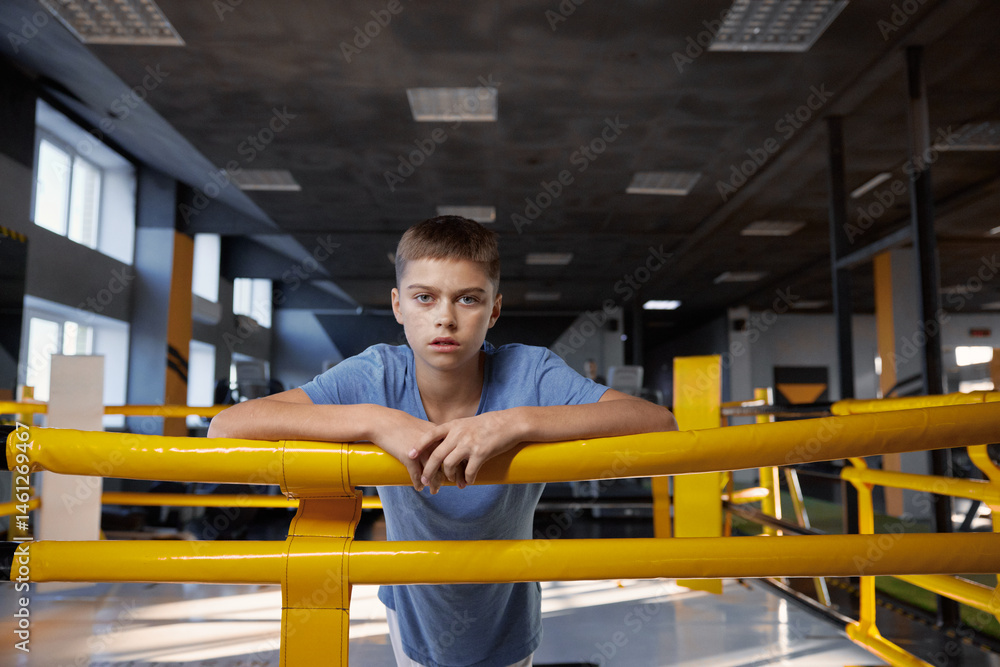 Portrait of tired teenage boy standing in boxing ring at modern gym