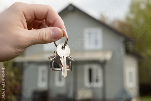 Foto Man hand holds house-shaped key in front of newly purchased home