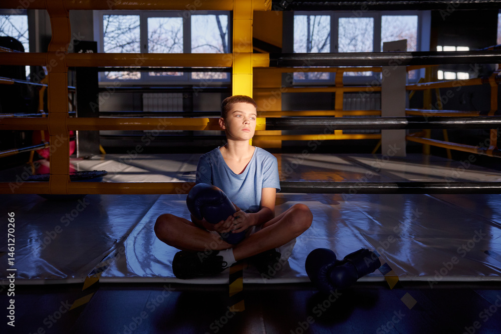 Teenage boy boxer resting after training inside boxing ring posing