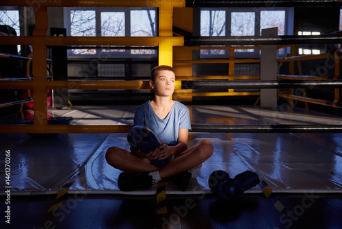 Teenage boy boxer resting after training inside boxing ring posing