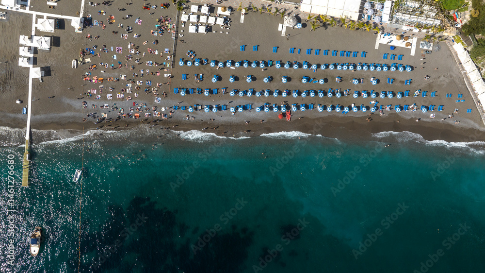 Perpendicular aerial view of the beach of Positano in the province of Salerno, Campania, Italy. There are umbrellas on the sand and people on vacation at sea.