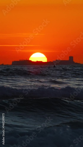 Puesta de sol en el mar con olas y castillo de fondo, Cádiz