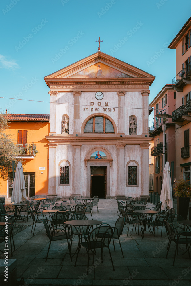 Fototapeta premium Front view of a church in the historic center of Intra, Verbania, surrounded by typical Italian buildings and outdoor café seating in a cozy piazza