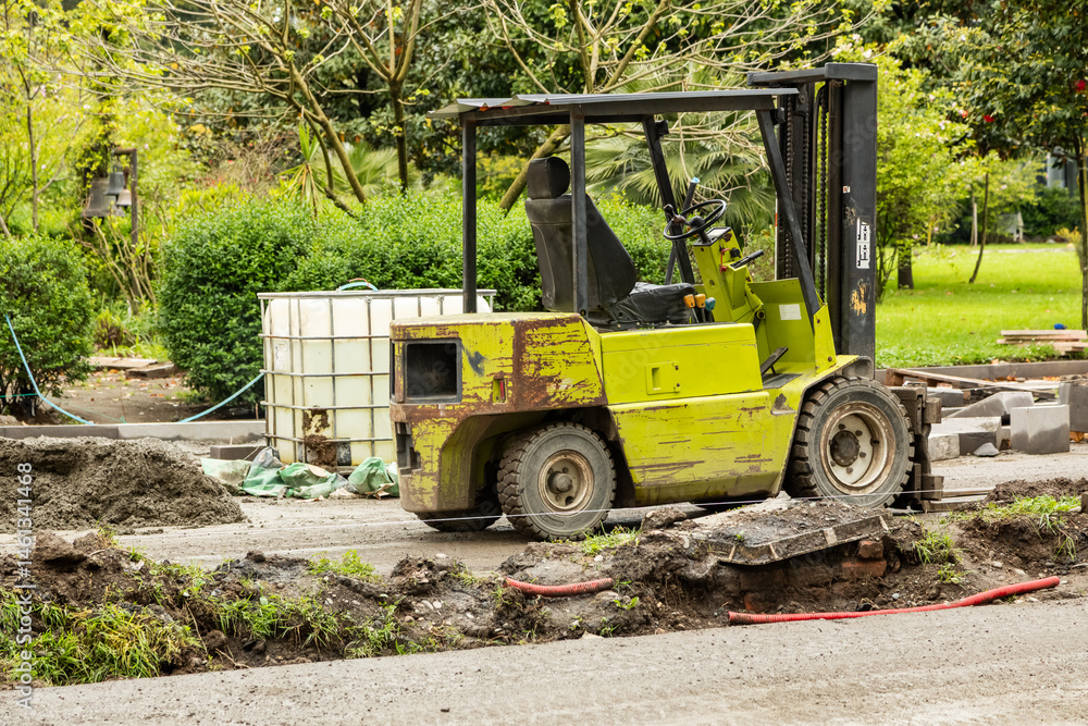 Rusty yellow forklift parked at urban construction site with tools, pipes and earth piles around during street renovation in green park area Rusty yellow forklift parked at urban construction site with tools, pipes and earth piles around during street renovation in green park area