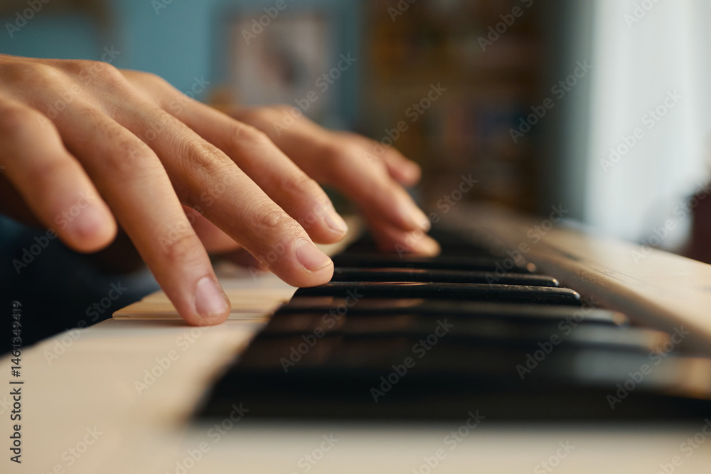 Fototapeta premium Close-up shot of hands playing on piano keys in a softly lit room, creating a warm and serene ambiance. The focus on the hands emphasizes the motion and skill involved in playing piano