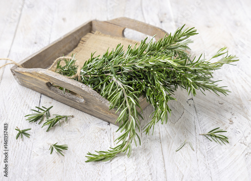 Obraz na płótnie Fresh green rosemary sprigs in a tray on white rustic table closeup. Aromatic herb for culinary w salonie