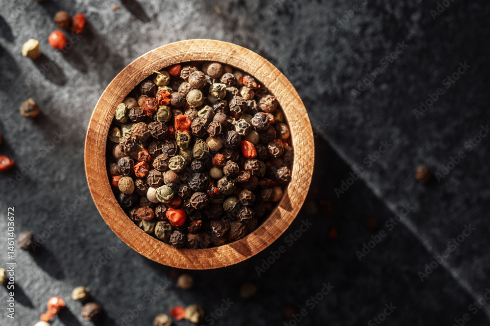 Colorful peppercorns in a wooden bowl on a dark surface with natural light