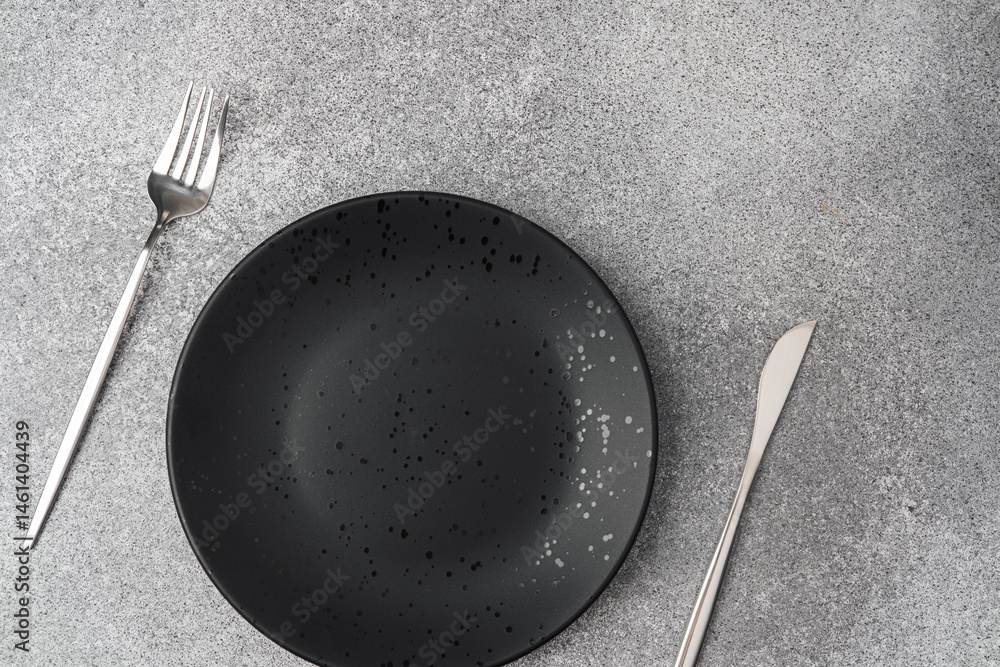 Elegant black plate with silver cutlery on a textured gray surface