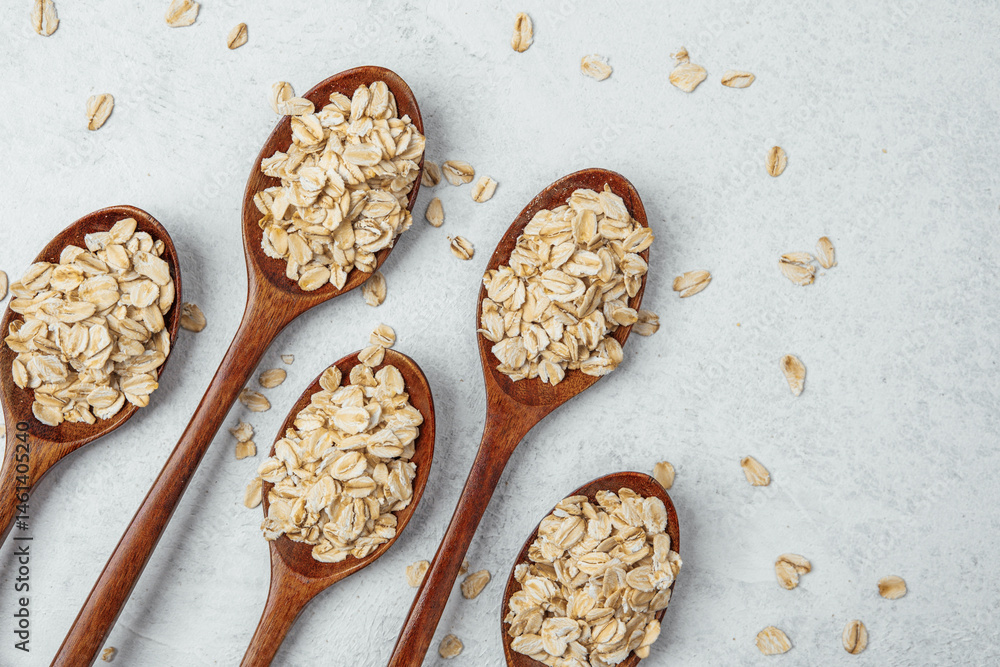 Oats arranged in wooden spoons on a light textured surface