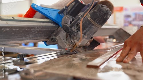A worker is cutting a ceramic tile on a wet cutter saw machine. Close-up