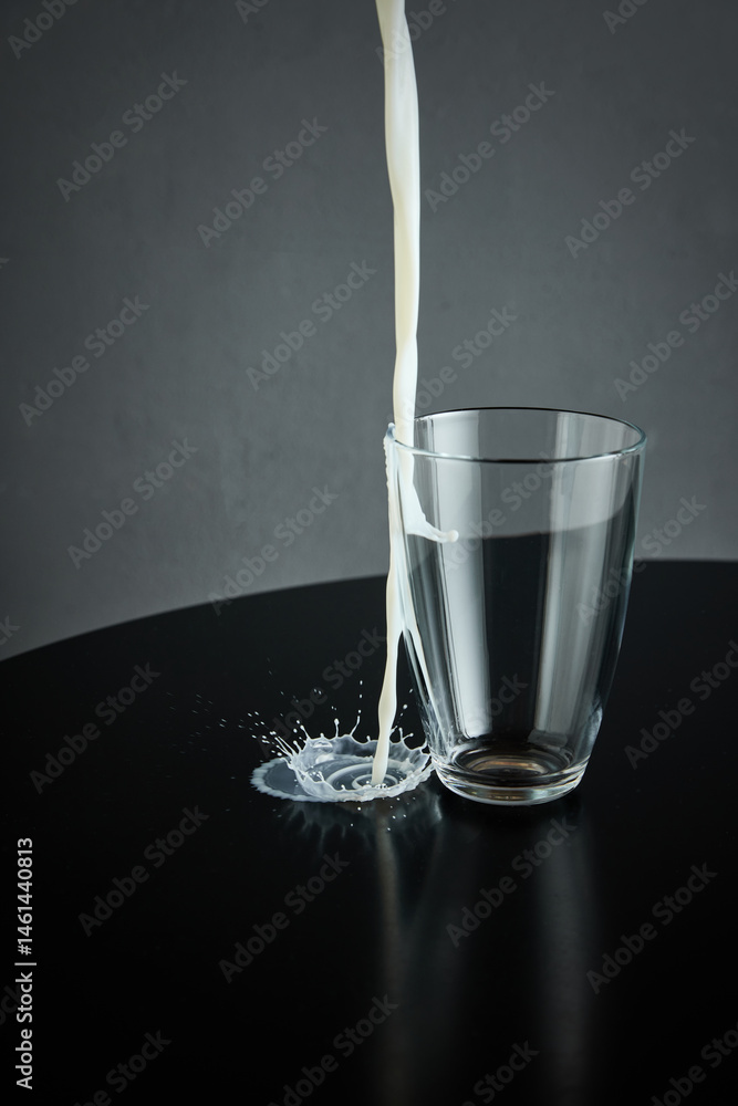 Milk misses transparent cup hitting black surface and creating dramatic splash. Concept of drink, organic food, aesthetics, advertisement