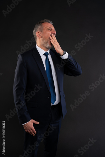 Businessman yawning while standing in formal suit.