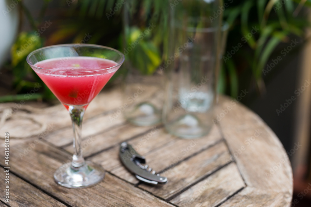 Red cocktail with ice in a stemmed glass on a wooden surface