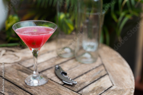 Red cocktail with ice in a stemmed glass on a wooden surface