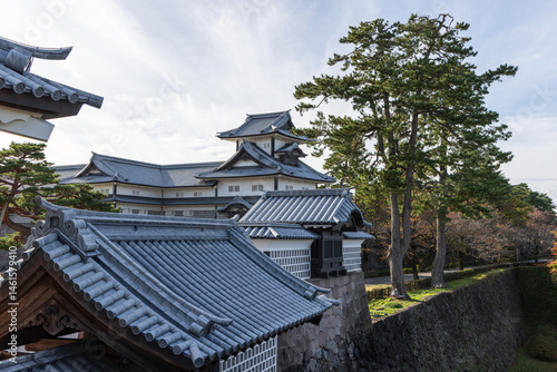 Traditional Japanese castle architecture at Kanazawa Castle with layered rooftops, fortified stone base, and green pine trees lining the outer perimeter path