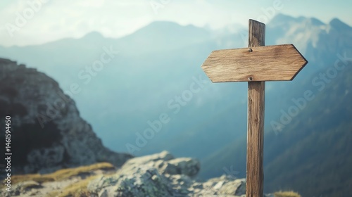 Wooden signpost points in two directions on a mountain trail with hazy peaks in the distance under a clear sky.