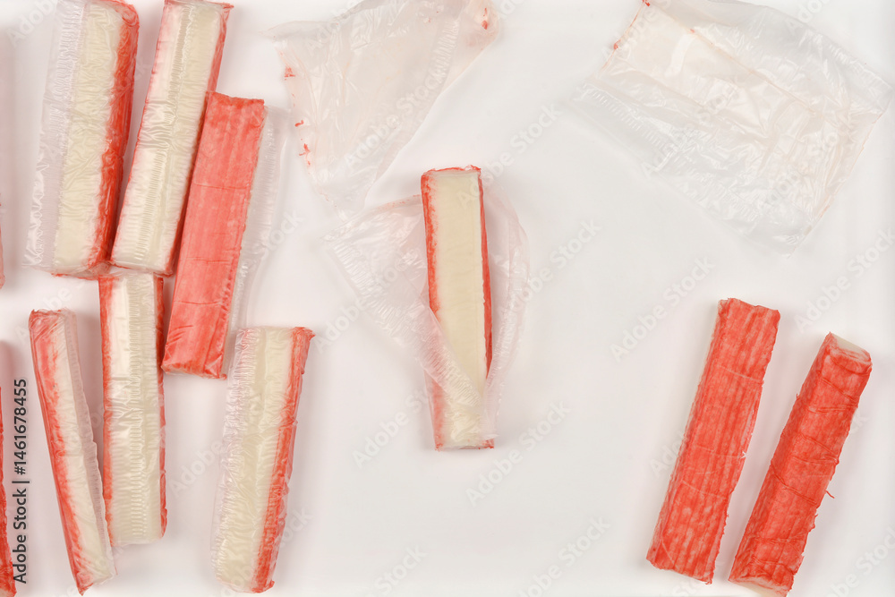 Several surimi sticks are arranged on a light surface, some in their original packaging and some unwrapped