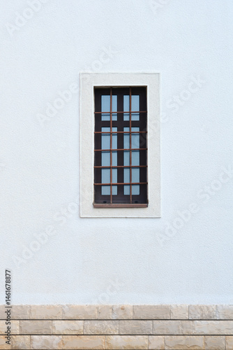 Obraz na płótnie A small, dark window with multiple panes and metal bars is set in a textured white wall above a stone foundation w salonie