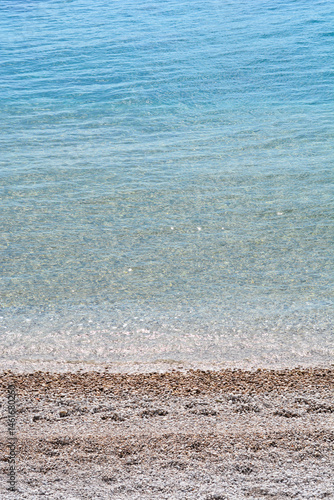 Obraz na płótnie Clear turquoise sea gently washes over a pebble beach under a bright sky w salonie