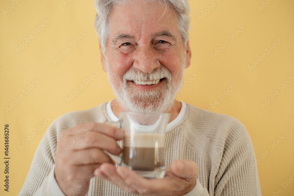 Close-up portrait of attractive bearded senior man holding a glass of coffee and milk, cappuccino, standing on yellow background looking at camera Close-up portrait of attractive bearded senior man holding a glass of coffee and milk, cappuccino, standing on yellow background looking at camera