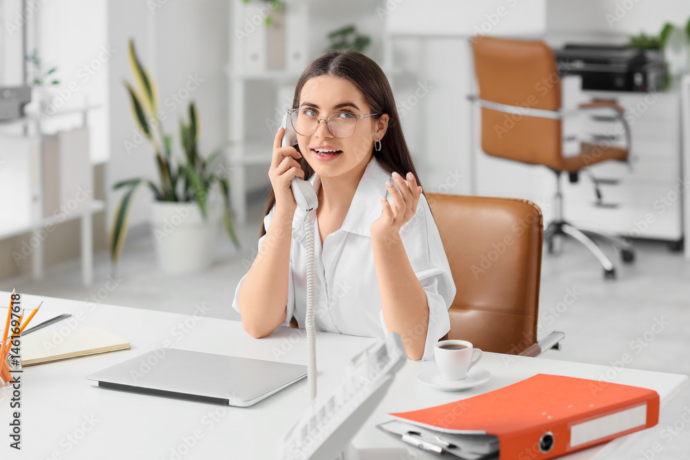 Obraz premium Young secretary talking by telephone at table in office