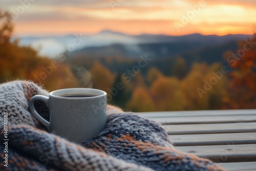 Warm coffee mug resting on a cozy blanket with a serene autumn sunset in the background