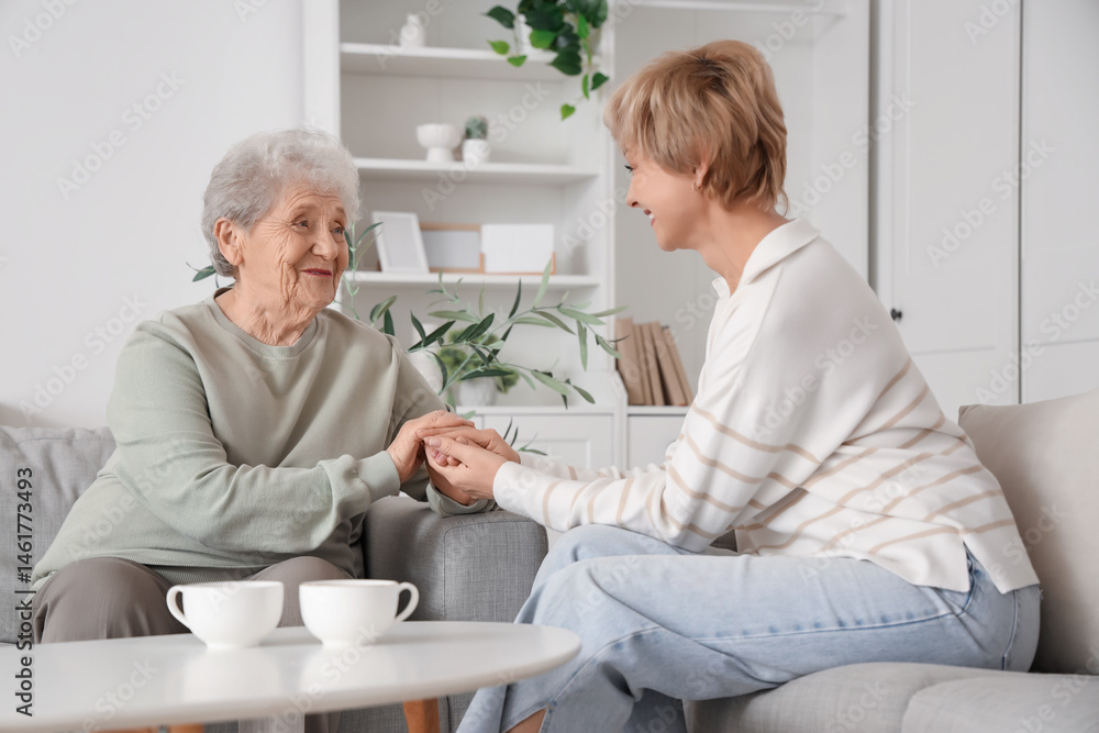 Fototapeta premium Mature woman with her mother holding hands on sofa at home