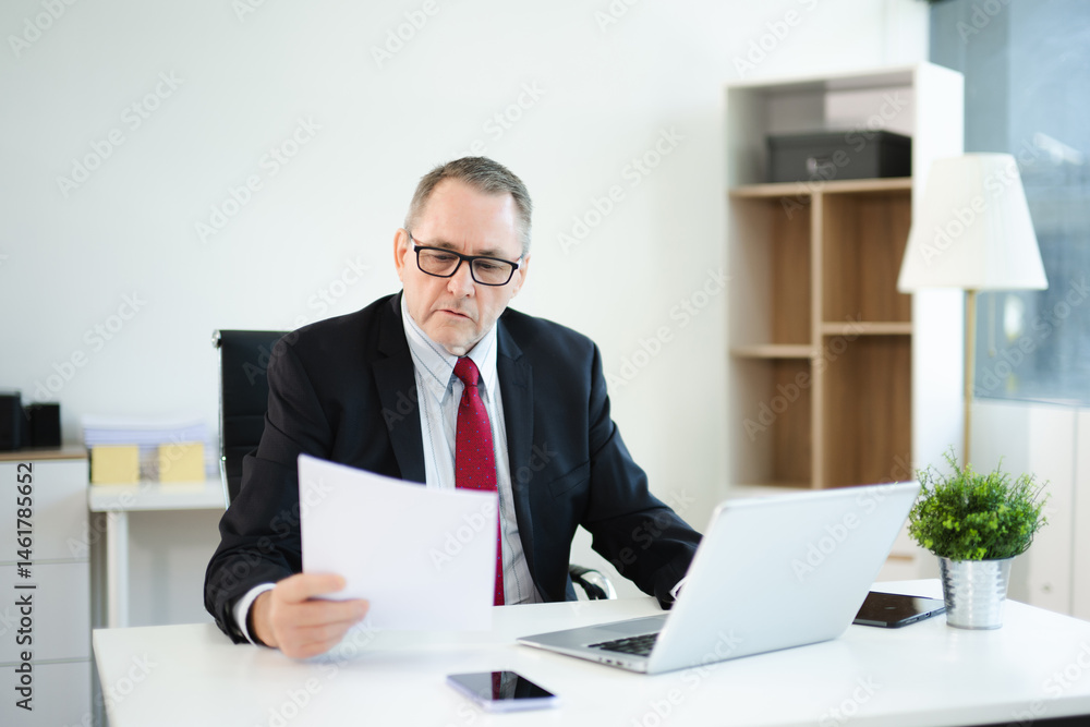 Confident businessman in suit, working on laptop and smartphone at office desk. Professional executive, leadership, strategy Confident businessman in suit, working on laptop and smartphone at office desk. Professional executive, leadership, strategy