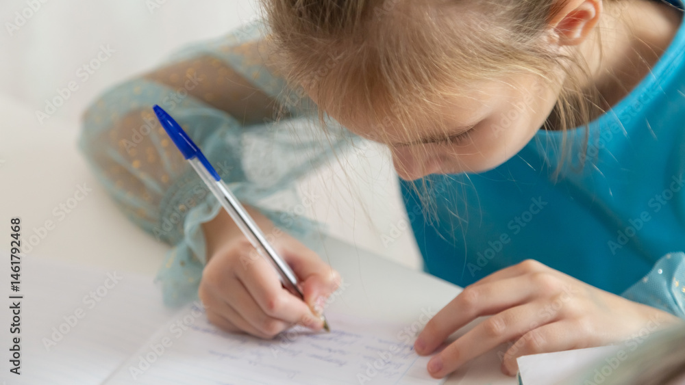 Little school girl sit at table at home write in exercise book prepare homework alone. Little school girl sit at table at home write in exercise book prepare homework alone.