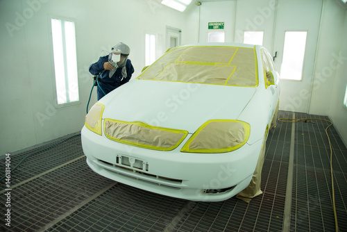 Auto painter in protective suit and mask, spraying a car in painting booth photo
