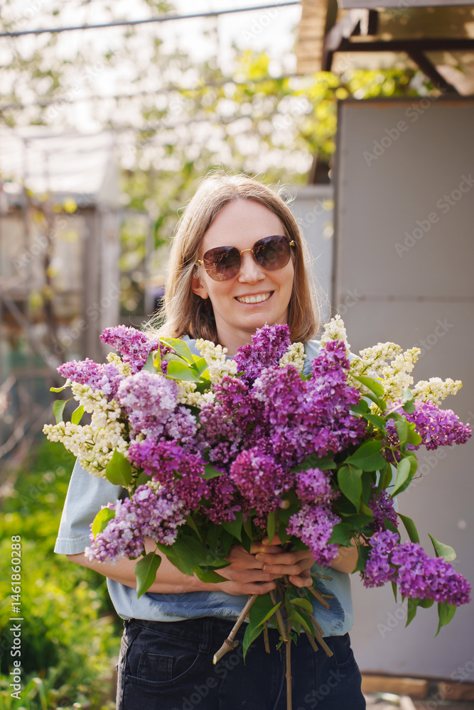Woman holding a large bouquet of lilacs in a sunny garden
