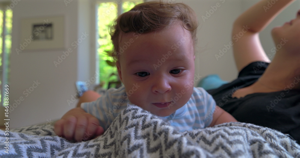 Baby lying on a blanket, looking slightly frustrated and emotional, in a warm home setting with natural light, while mother observes in the background Baby lying on a blanket, looking slightly frustrated and emotional, in a warm home setting with natural light, while mother observes in the background