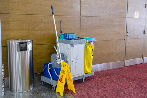 Janitorial cleaning cart with mop, bucket, and caution sign in a commercial building hallway. The image highlights tools and equipment used for professional cleaning services